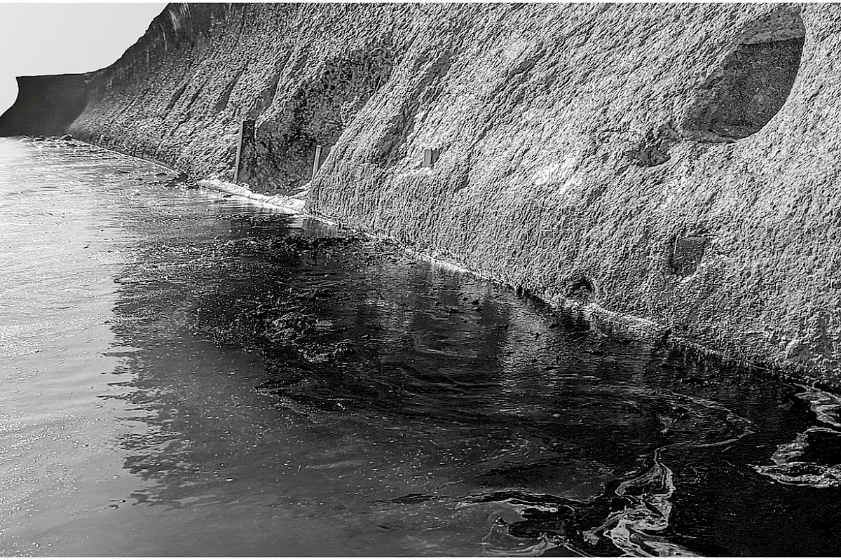 Oil in the water that has seeped from a seawall where there once were wells and oil storage tanks, and now a residence.